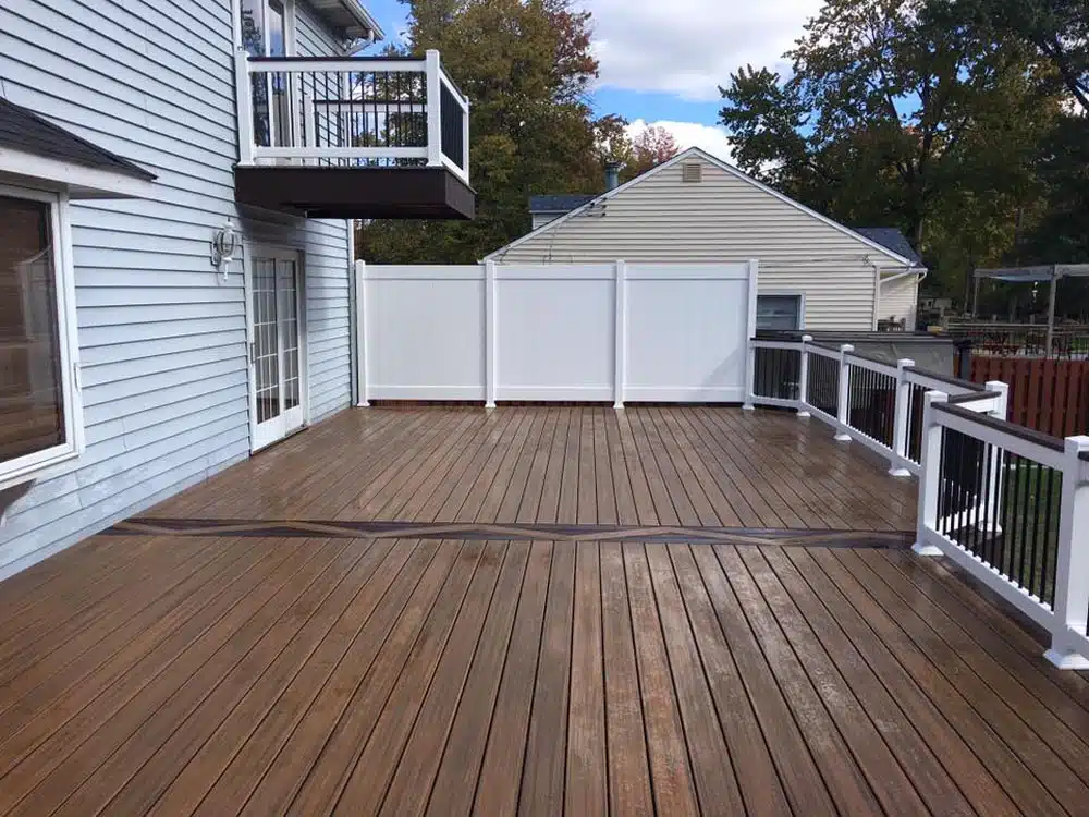 Wooden deck with white railings, overlooking a fenced backyard.