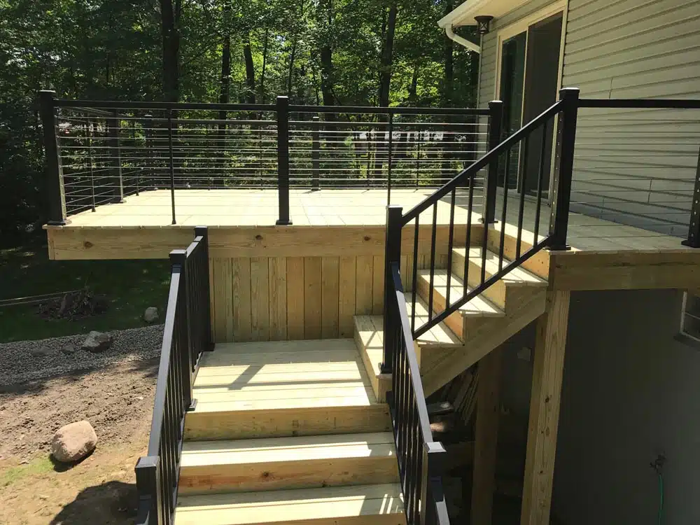 Stairs leading up to an elevated deck with black railings photo - Hen House Decks