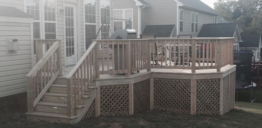 Empty wooden deck with white railing and black spindles, connected to a beige house photo - House Hen Decks