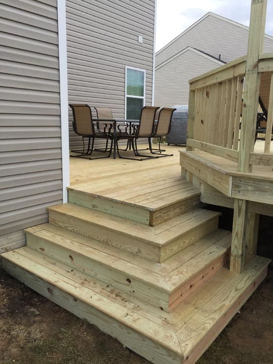 Elevated wooden deck with stairs and a handrail leading down to a grassy lawn.