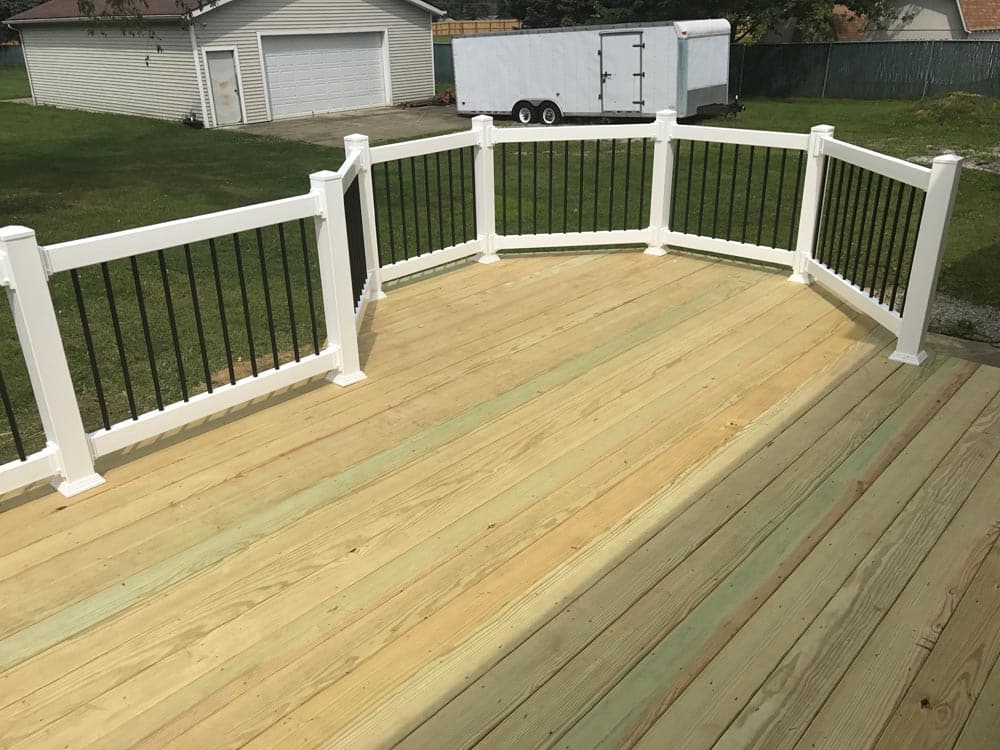 Completed wooden deck with white railing and stairs leading to a backyard