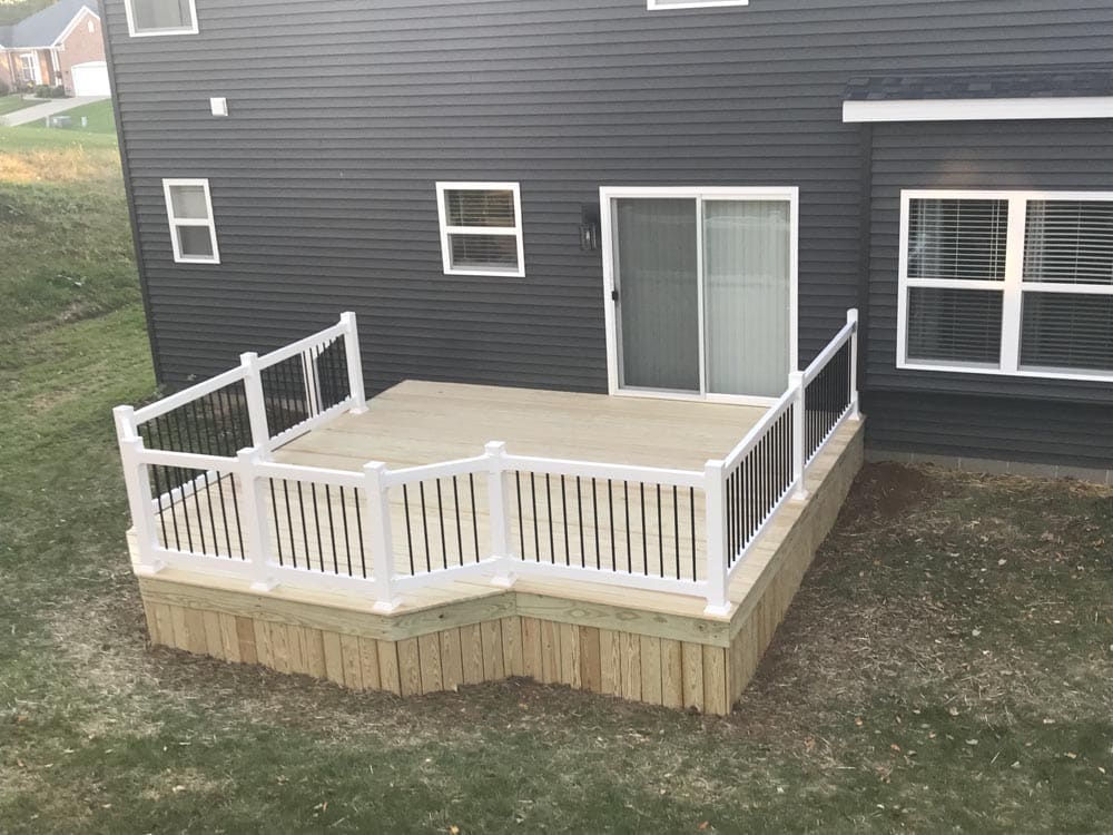 Corner view of a deck with white railings and stairs leading to a yard.