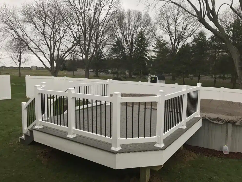 Small wooden deck with white railings attached to a house with grey siding.