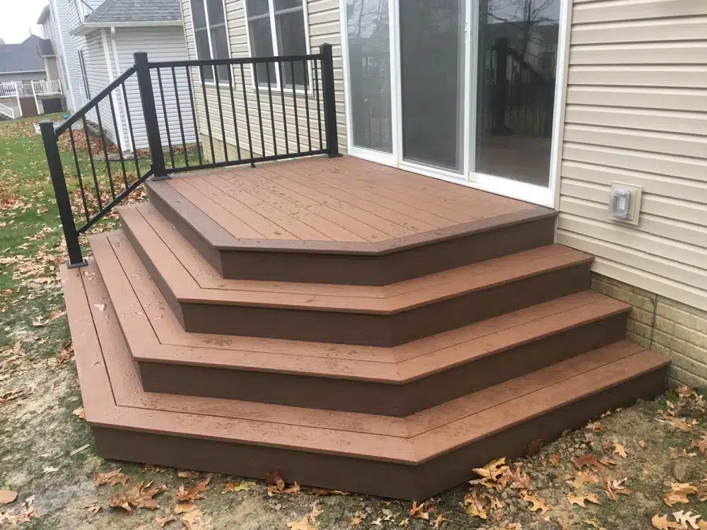 Brown wooden steps leading up to a deck with no railings, attached to a house.