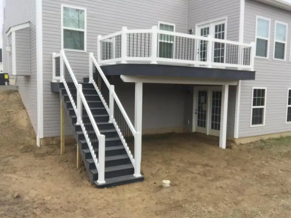 House with an elevated white deck and staircase leading to a gravel backyard.