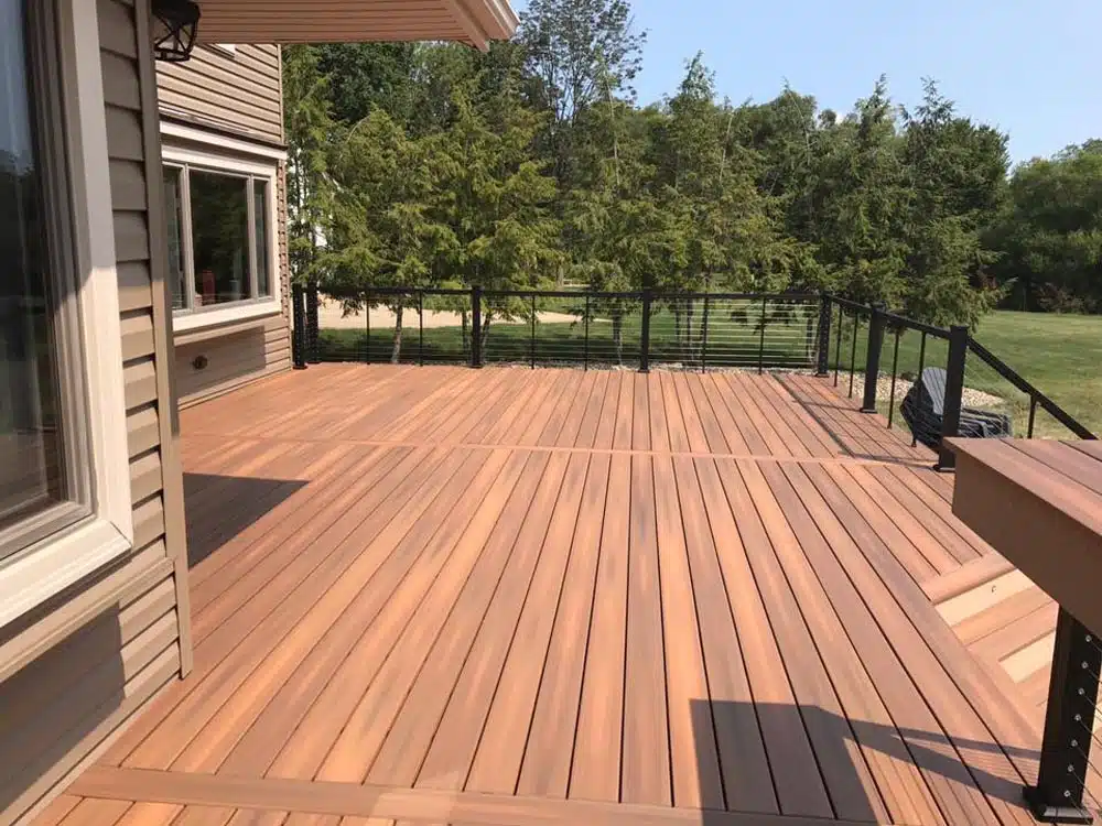 Freshly built wooden deck without railings, leading to a white house with black shutters.