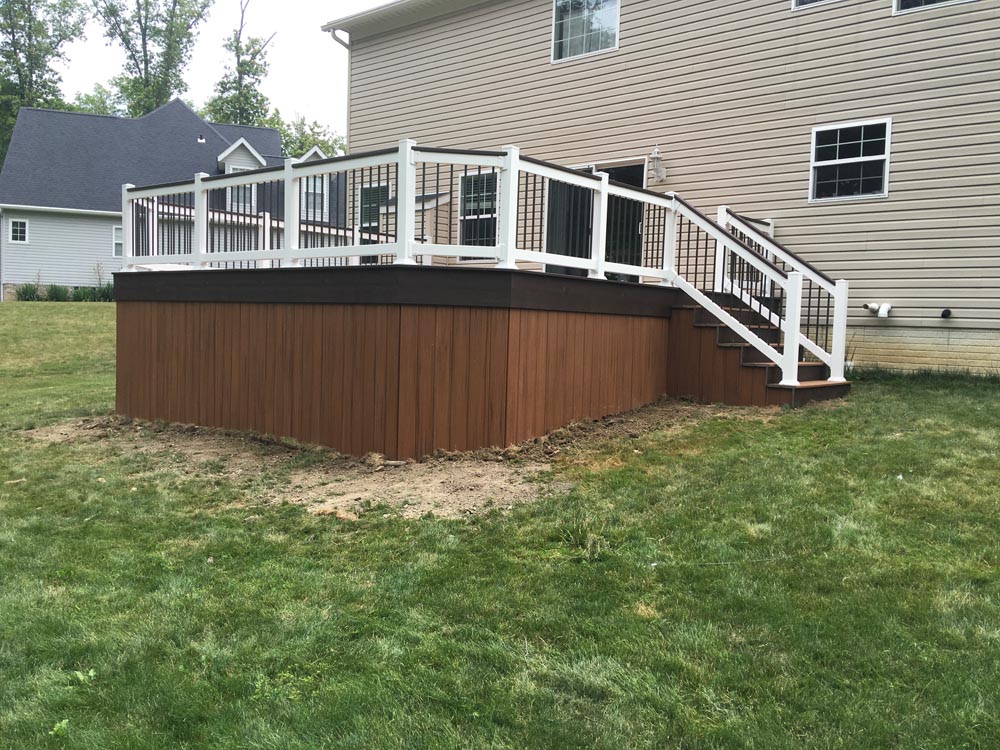 Elevated, curved wooden deck with a railing and steps leading to a grassy yard