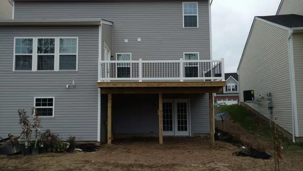 Elevated wooden deck with white railings and support beams, under construction.