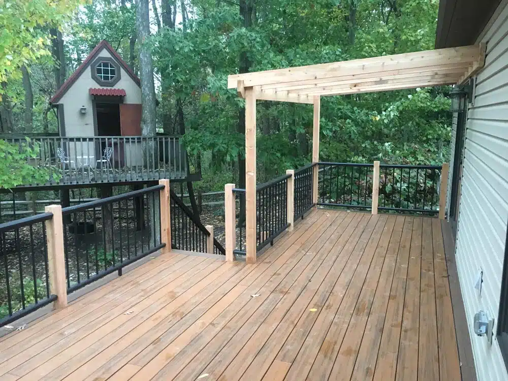 Wooden deck with a pergola overhead and trees in the background.
