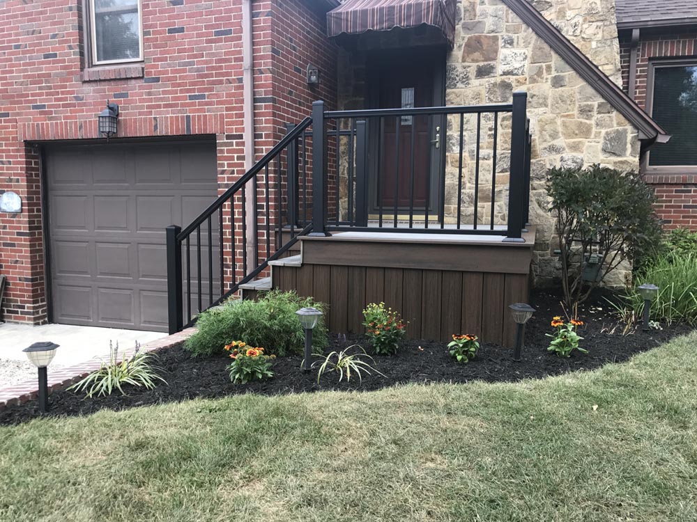 Small black metal balcony with stairs leading down to a backyard garden.