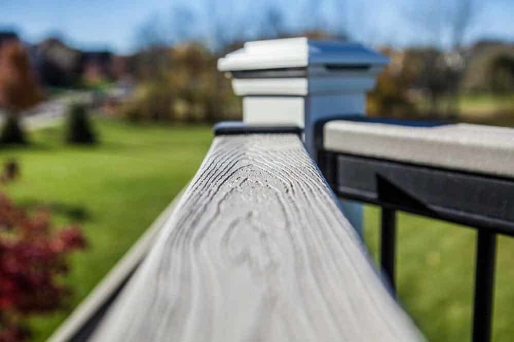 Close-up of a wooden deck railing with a blurred green landscape in the background.
