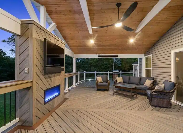 Covered wooden deck illuminated at dusk, with seating and an outdoor rug.