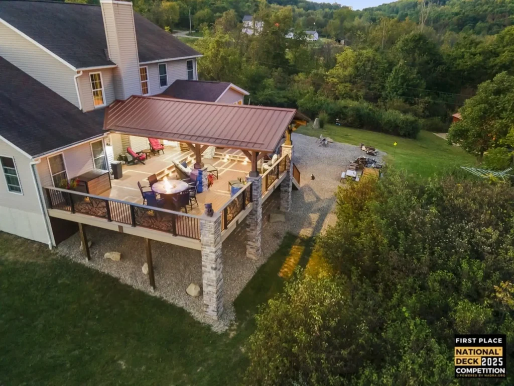 Home 7 screened porch vs deck: elevated covered deck with metal roof, stone support columns, outdoor dining seating and fire table overlooking a wooded backyard